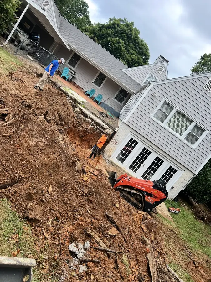 Compact excavator working a steep slope behind a house